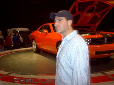 1970 Ford Ranchero - A man stands next to a bright orange muscle car on display, with its hood raised to show the engine.