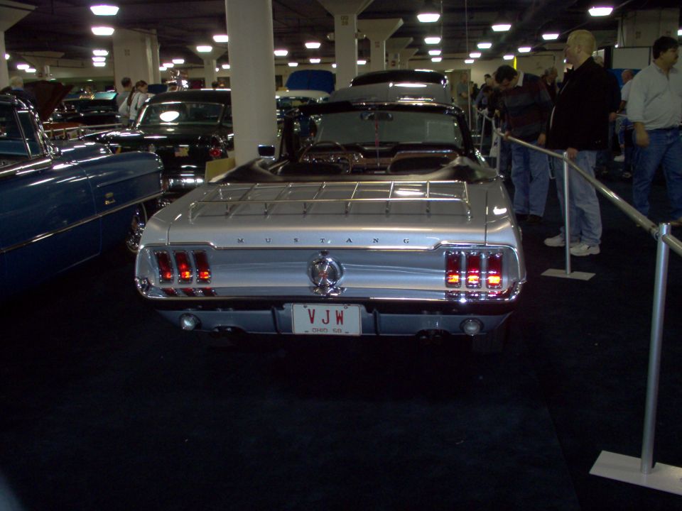 Rear of a silver classic Ford Mustang convertible at an indoor car show
