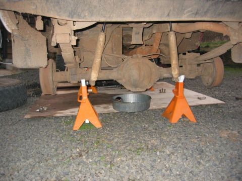 1991 Ford Explorer - The underside of a vehicle is shown, supported by jack stands, with a drain pan positioned below the rear axle.