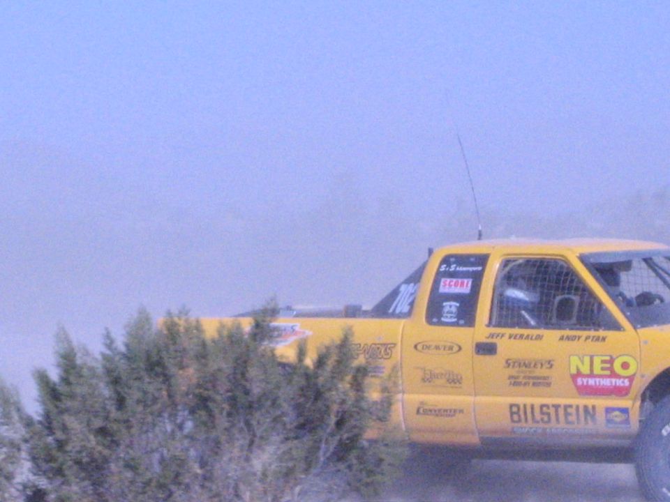 Yellow off-road race truck covered in sponsor decals on a dusty course