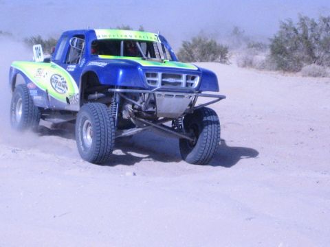 Blue and green off-road race truck number 104 on a desert course