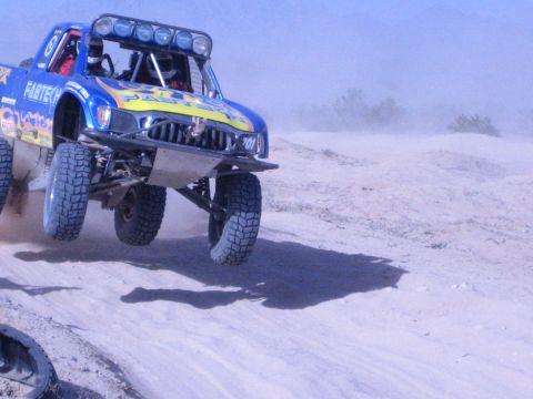 Blue and yellow off-road race truck airborne over a desert berm
