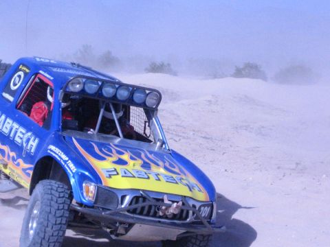 Blue Fabtech-liveried off-road race truck with flames on a desert dune