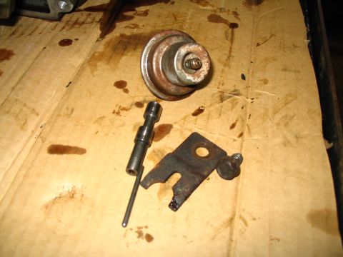 1984 Ford Bronco - A transmission vacuum modulator and linkage are shown disassembled on a stained cardboard surface.