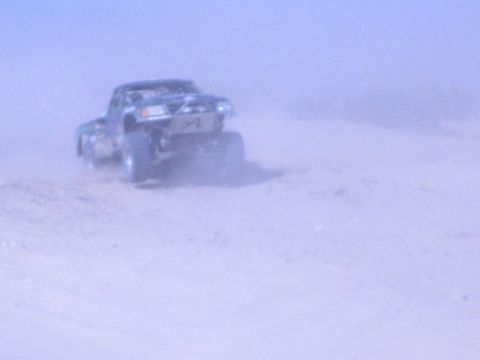 Off-road race truck speeding away through a thick desert dust cloud