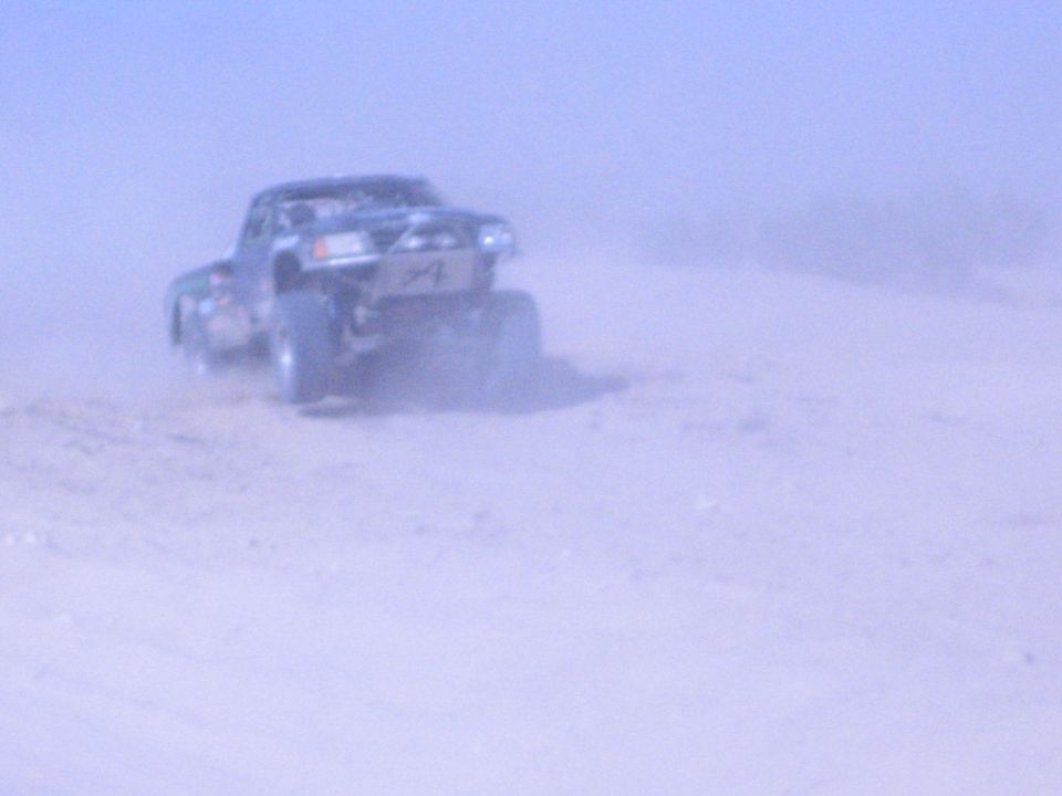 Off-road race truck speeding away through a thick desert dust cloud