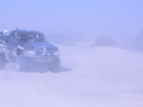 Blue off-road race truck kicking up dust on a desert sand course