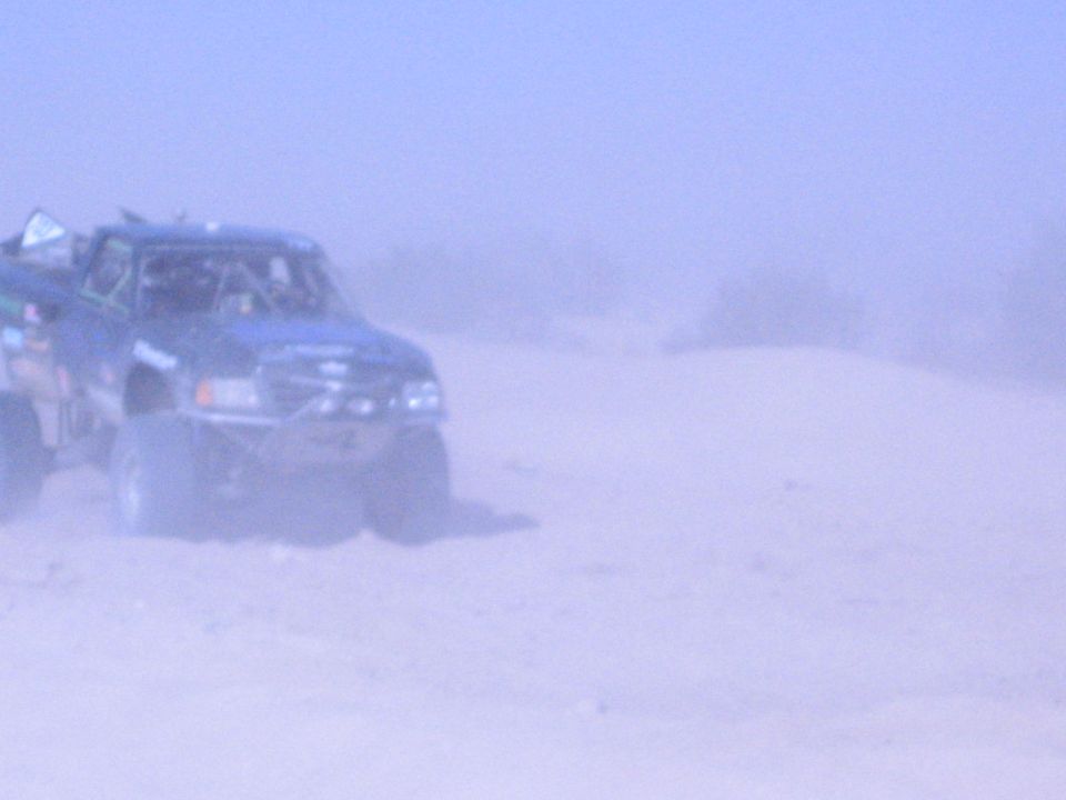 Blue off-road race truck kicking up dust on a desert sand course