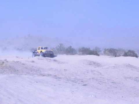 Yellow off-road race truck cresting a sand dune in dusty desert