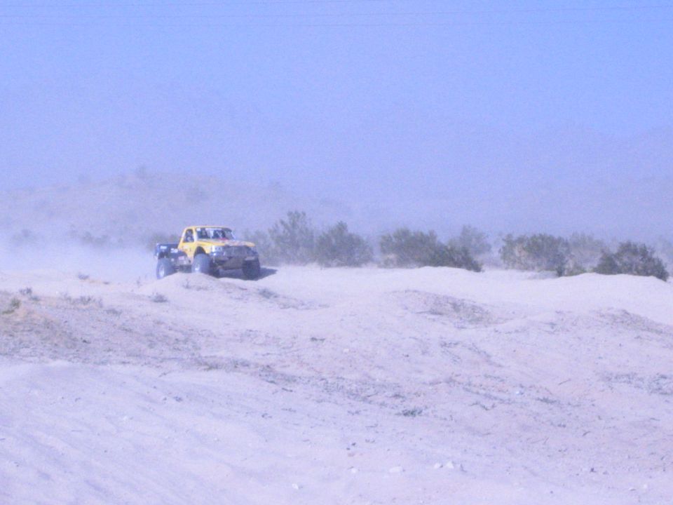 Yellow off-road race truck cresting a sand dune in dusty desert