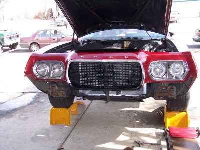 1972 Ford Ranchero - The front end of a red 1972 Ford Ranchero is shown with its hood open, elevated on yellow jack stands.