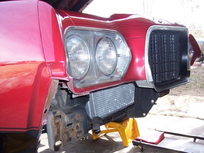 1972 Ford Ranchero - The front of a red vehicle is shown with its hood up, supported by jack stands, revealing an intercooler installation.