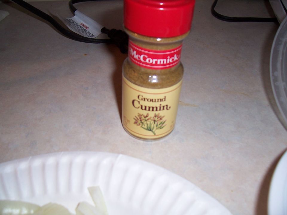 McCormick Ground Cumin spice bottle with red cap, on a counter next to sliced onions