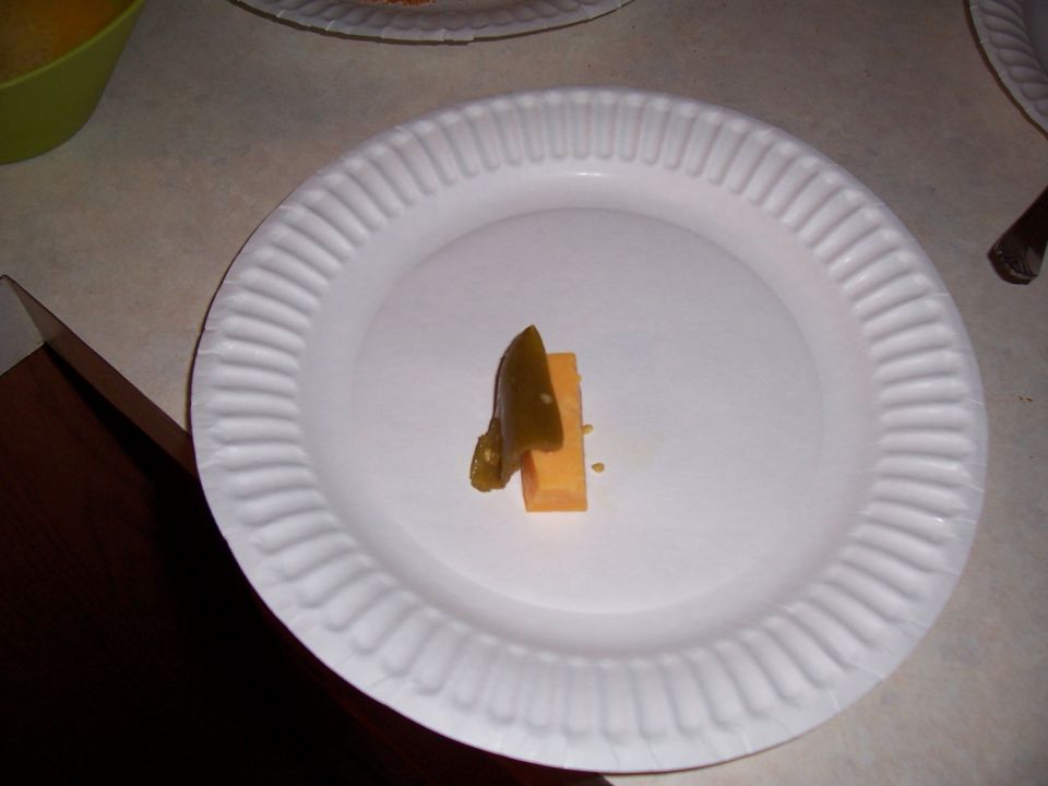 Piece of cheese with a jalapeno slice on top, on a paper plate