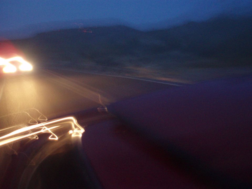Blurry dusk shot of a road with oncoming headlights and a red car hood