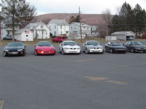 2002 Chevrolet Camaro - A line of six sports cars, including a black 2002 Chevrolet Camaro, are parked in a lot.