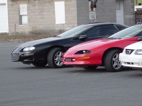 2002 Chevrolet Camaro - Three sports cars, including a black 2002 Chevrolet Camaro, are parked in a lot.