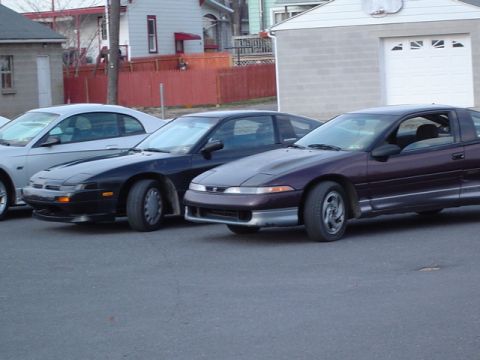 2002 Chevrolet Camaro - Three coupes are parked in a lot, with a garage and houses in the background.