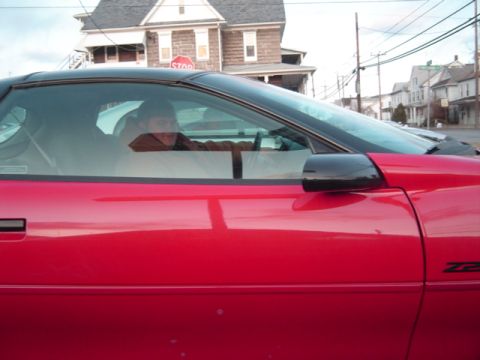 2002 Chevrolet Camaro - A red sports car with a black top is parked on a street with houses in the background.