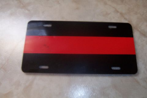 1998 Ford Crown Victoria - A black license plate with a single red stripe across the middle is shown against a textured background.