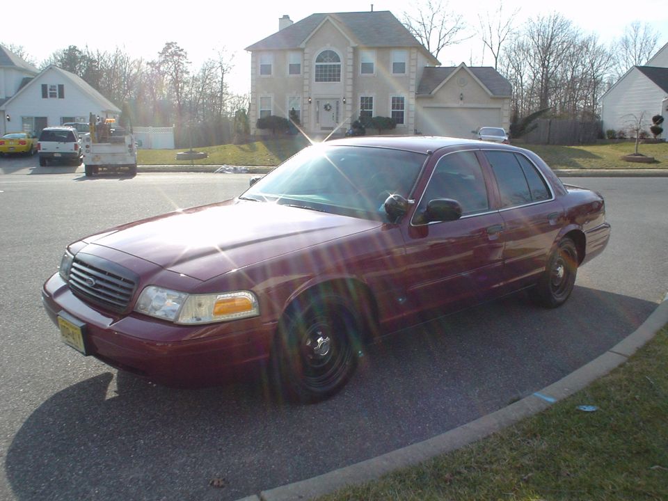 Burgundy Crown Victoria sedan with black steel wheels parked on suburban street, front 3/4 view