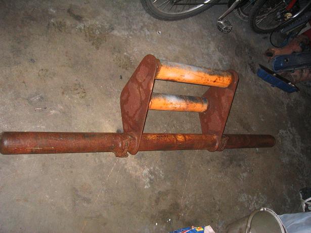 Rusty steel tubular fabricated part with orange cross tubes on concrete floor