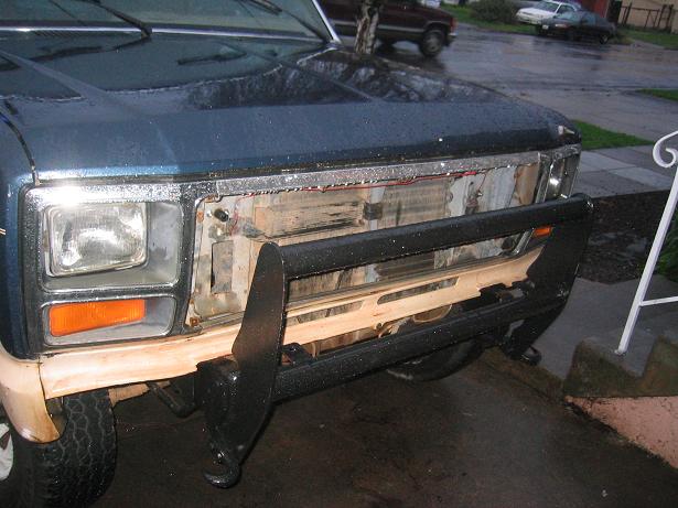 Front of dark blue Bronco with grille removed, exposed radiator area, black tube brush guard, wet from rain