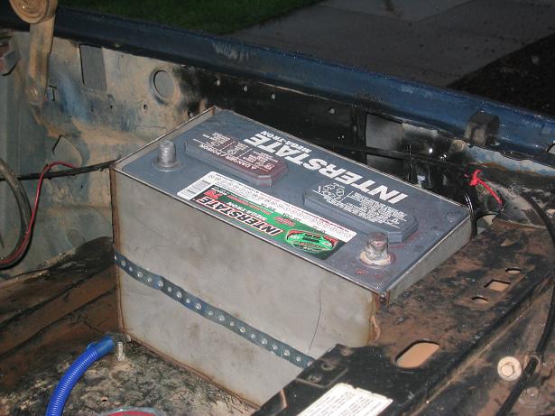 Interstate battery on a metal tray with strap in the bare engine bay of a 1986 Ford Bronco