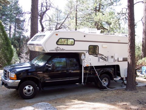 2000 Ford F-250 - A black Ford F-250 truck is equipped with a white Alpenlite camper, parked outdoors among trees.