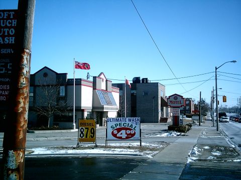 1997 Ford Escort - A street scene a motel, gas prices, and car wash advertisement under a clear blue sky.