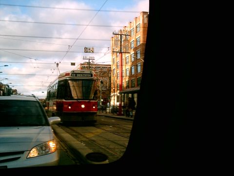 1997 Ford Escort - A streetcar and a car are seen on a city street with buildings in the background.