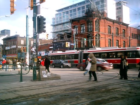 1997 Ford Escort - A busy street intersection in Toronto features a tram, several cars, and pedestrians crossing the road.