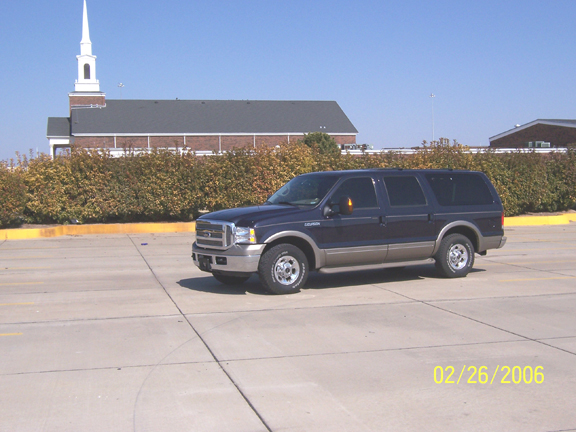 Blue Ford Excursion SUV front three-quarter in a lot by a white church steeple