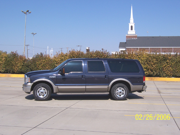 Blue two-tone Ford Excursion SUV side profile in a parking lot by a church