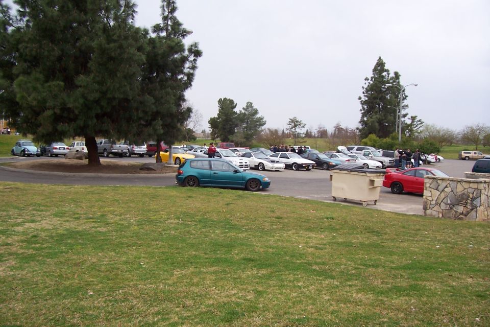 teal hatchback parked in front of a lot full of cars under a cloudy sky