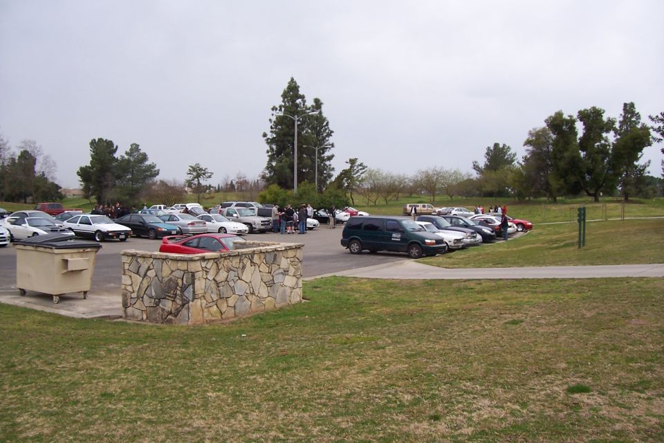 Parking lot with many cars and a green van, stone wall, and dumpster