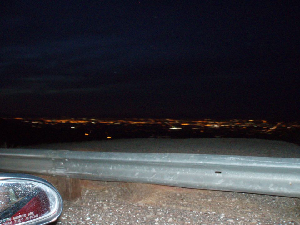 Distant city lights at night beyond a guardrail and a car's side mirror