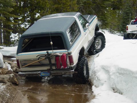 1986 Ford Bronco - A white Ford Bronco navigates a snowy and muddy trail, with another vehicle visible in the background.