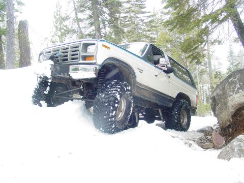 1986 Ford Bronco - 1986 Ford Bronco navigates a snowy, rocky trail in a wooded area.