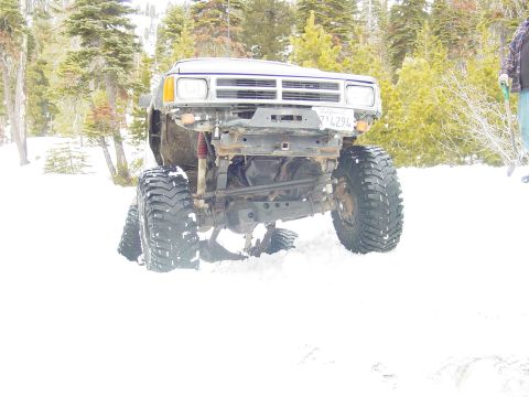 1986 Ford Bronco - A heavily modified truck with oversized tires is stuck in the snow, seen from the front.