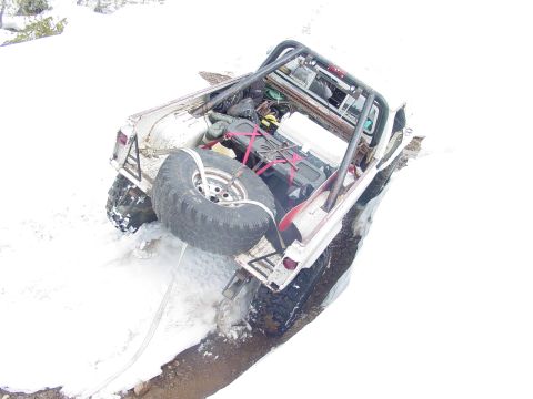 1986 Ford Bronco - Off-road Bronco stuck in snow, showing its rear and spare tire. Winch line is attached.