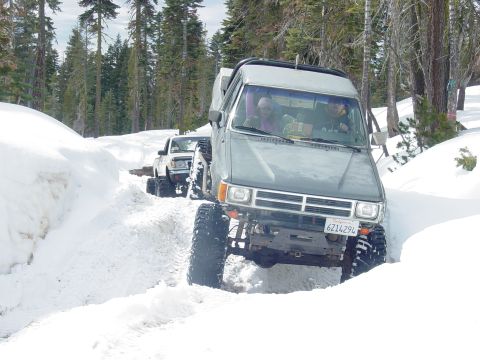 1986 Ford Bronco - Two off-road vehicles navigate a snow-covered path through a forest.