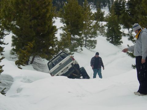 1986 Ford Bronco - A white pickup truck is stuck in a snow drift with two people observing the scene.