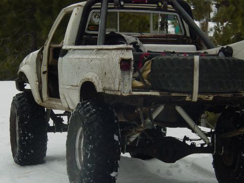 1986 Ford Bronco - Off-road pickup truck with significant suspension modifications and large tires sits in a snowy landscape.