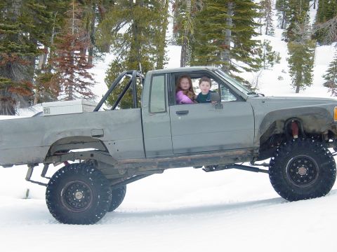 1986 Ford Bronco - This heavily modified pickup truck is parked in the snow with two children inside.