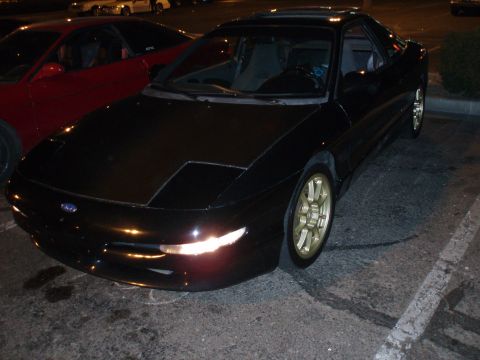 1997 Ford Probe - A black coupe with pop-up headlights and gold rims is parked in a lot next to a red car.