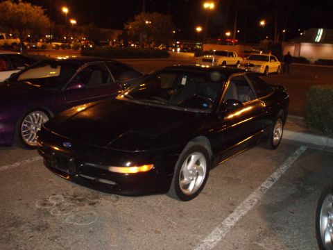 1997 Ford Probe - A black 1997 Ford Probe is parked in a lot at night, with other vehicles visible in the background.
