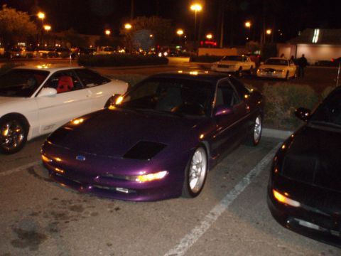 1997 Ford Probe - A purple sports car is parked in a lot at night, alongside other vehicles.