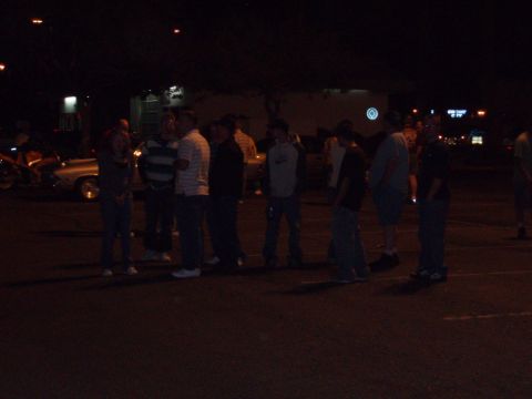 1997 Ford Probe - People socializing around vehicles in a parking lot after dark.