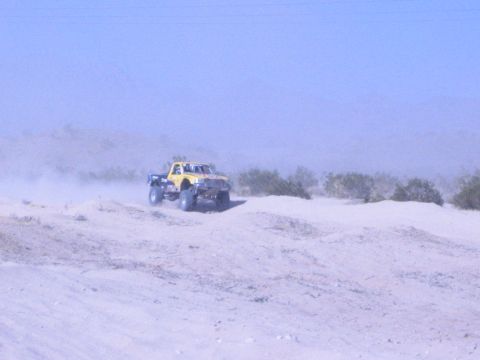 Yellow desert race truck on a sandy ridge with brush and dust